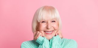 Eine fröhliche Seniorin mit einem strahlend weißen Lächeln auf pinkem Hintergrund.