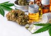 Auf einem weißen Tisch stehen und liegen verschiedene CBD Produkte, wie CBD Öl, CBD Blüten und CBD Kapseln.