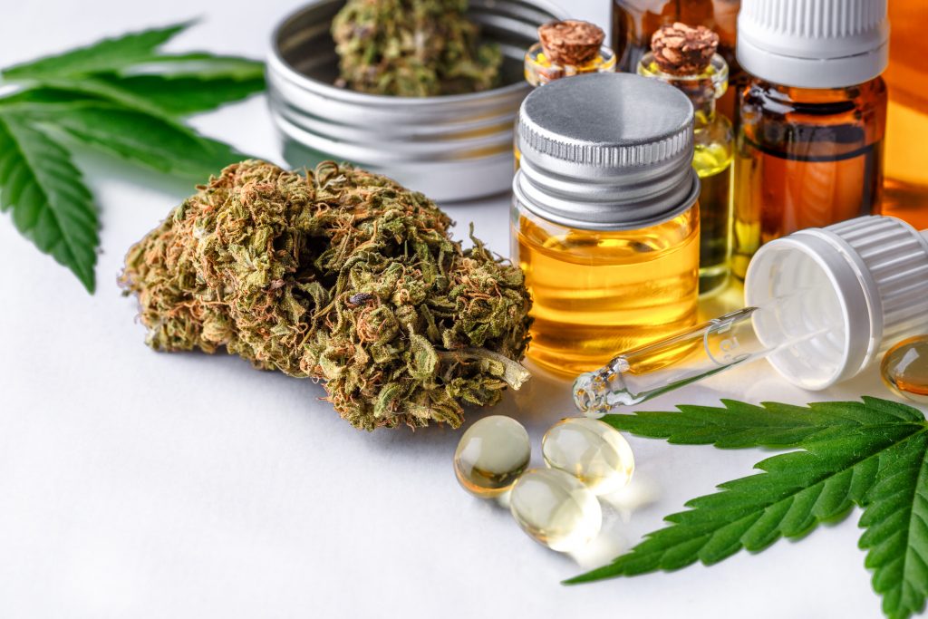 Auf einem weißen Tisch stehen und liegen verschiedene CBD Produkte, wie CBD Öl, CBD Blüten und CBD Kapseln.
