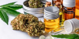 Auf einem weißen Tisch stehen und liegen verschiedene CBD Produkte, wie CBD Öl, CBD Blüten und CBD Kapseln.