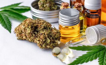 Auf einem weißen Tisch stehen und liegen verschiedene CBD Produkte, wie CBD Öl, CBD Blüten und CBD Kapseln.