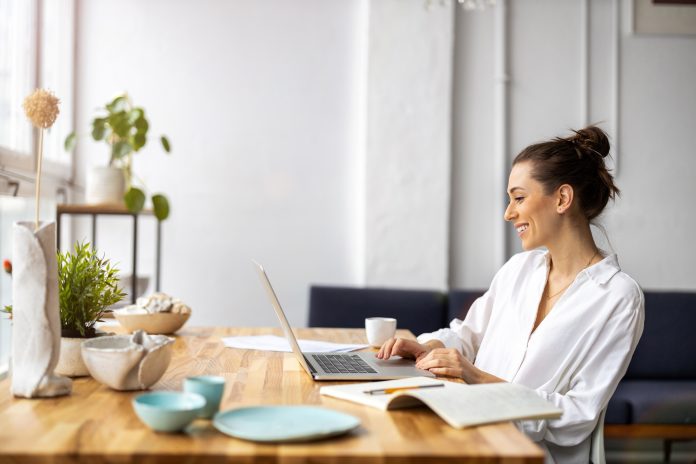 Home Office Rückenschmerzen Frau sitzt im Wohnzimmer am Schreibtisch und arbeitet.