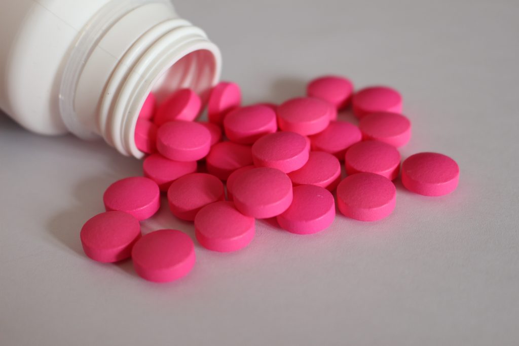 Rosa Tabletten aus einer geöffneten Medikamentenflasche als Symbol für Schmerzmittel bei chronischen Beschwerden.