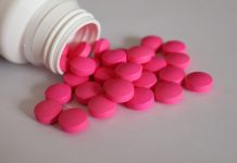 Rosa Tabletten aus einer geöffneten Medikamentenflasche als Symbol für Schmerzmittel bei chronischen Beschwerden.