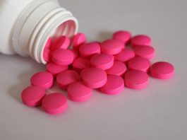 Chronische Beschwerden lindern: Wie alternative Therapieformen die Medikamentenbelastung senken können Rosa Tabletten aus einer geöffneten Medikamentenflasche als Symbol für Schmerzmittel bei chronischen Beschwerden.