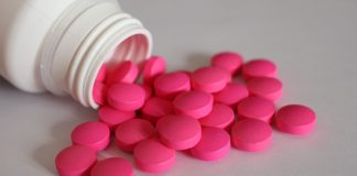 Rosa Tabletten aus einer geöffneten Medikamentenflasche als Symbol für Schmerzmittel bei chronischen Beschwerden.