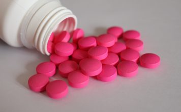 Rosa Tabletten aus einer geöffneten Medikamentenflasche als Symbol für Schmerzmittel bei chronischen Beschwerden.