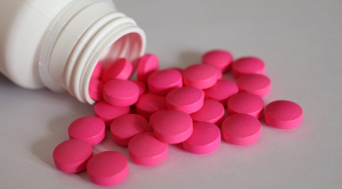 Rosa Tabletten aus einer geöffneten Medikamentenflasche als Symbol für Schmerzmittel bei chronischen Beschwerden.