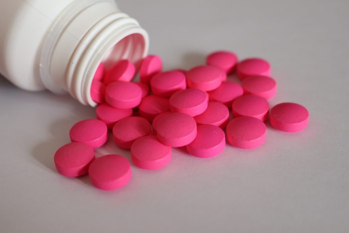 Rosa Tabletten aus einer geöffneten Medikamentenflasche als Symbol für Schmerzmittel bei chronischen Beschwerden.