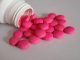 Rosa Tabletten aus einer geöffneten Medikamentenflasche als Symbol für Schmerzmittel bei chronischen Beschwerden.