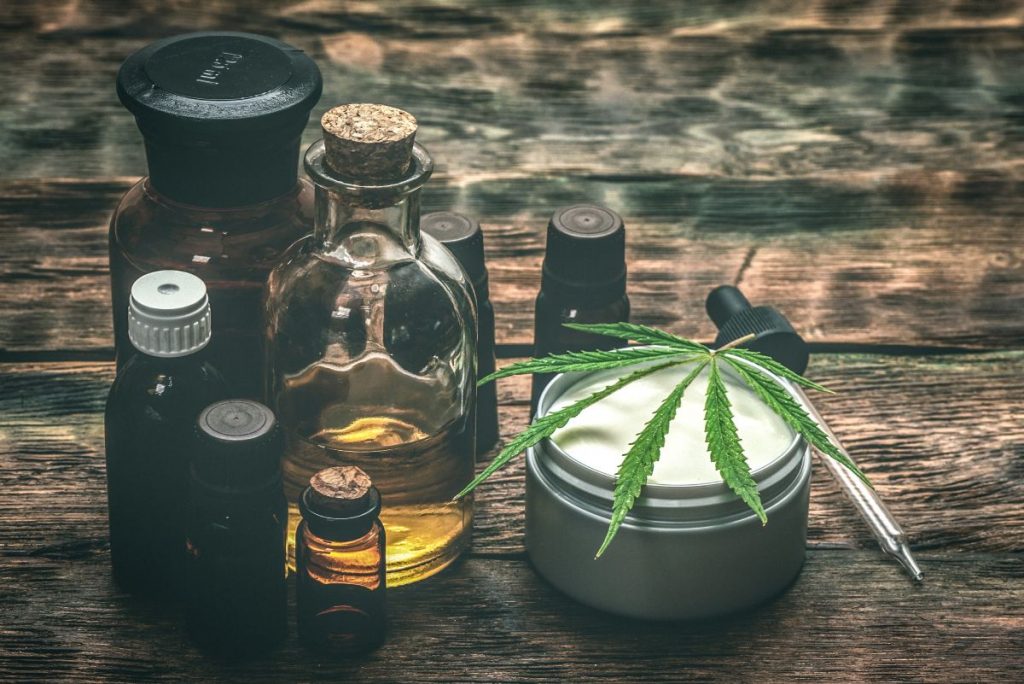 Verschiedene CBD-Produkte auf Holztisch, darunter Ölflaschen, Cremedose mit Hanfblatt und Pipette – Symbol für natürliche Anwendungen von Cannabidiol zur Unterstützung von Gesundheit und Wohlbefinden.