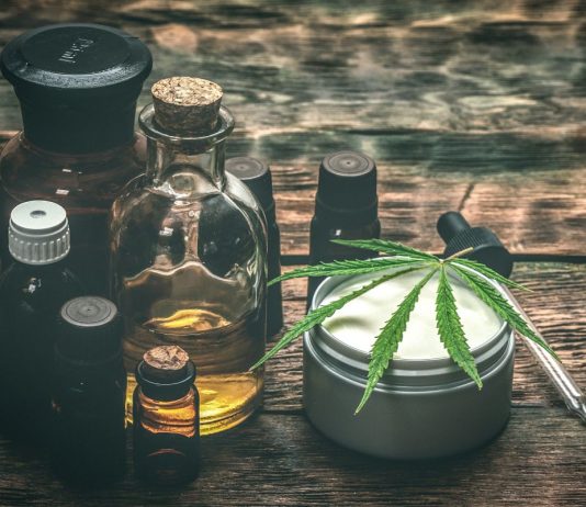 Verschiedene CBD-Produkte auf Holztisch, darunter Ölflaschen, Cremedose mit Hanfblatt und Pipette – Symbol für natürliche Anwendungen von Cannabidiol zur Unterstützung von Gesundheit und Wohlbefinden.