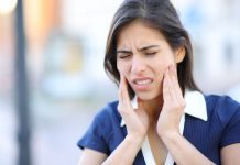 Frau mit Schmerzen im Kieferbereich fasst sich an beide Wangen – typisches Symptom bei CMD (Craniomandibuläre Dysfunktion) oder Kiefergelenksbeschwerden.