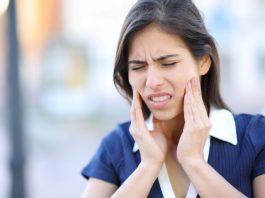 Frau mit Schmerzen im Kieferbereich fasst sich an beide Wangen – typisches Symptom bei CMD (Craniomandibuläre Dysfunktion) oder Kiefergelenksbeschwerden.