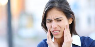 Frau mit Schmerzen im Kieferbereich fasst sich an beide Wangen – typisches Symptom bei CMD (Craniomandibuläre Dysfunktion) oder Kiefergelenksbeschwerden.
