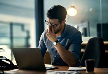 Auswirkungen anhaltend hoher Cortisolspiegel auf den Alterungsprozess Ein Mann sitzt gestresst am Schreibtisch vor seinem Laptop und reibt sich die Augen – Symbolbild für beruflichen Stress, Überlastung und erhöhte Cortisolwerte durch dauerhafte Anspannung.