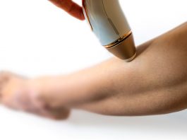 Frau wendet ein IPL-Gerät zur dauerhaften Haarentfernung am Unterschenkel an. Nahaufnahme der Behandlung, Fokus auf Haut und Handgerät für glatte, haarfreie Beine.