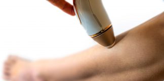 Frau wendet ein IPL-Gerät zur dauerhaften Haarentfernung am Unterschenkel an. Nahaufnahme der Behandlung, Fokus auf Haut und Handgerät für glatte, haarfreie Beine.