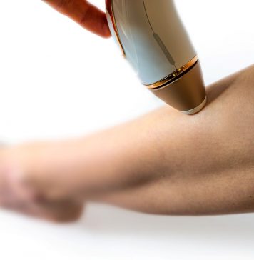 Frau wendet ein IPL-Gerät zur dauerhaften Haarentfernung am Unterschenkel an. Nahaufnahme der Behandlung, Fokus auf Haut und Handgerät für glatte, haarfreie Beine.