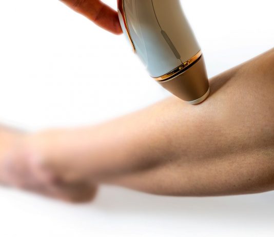 Frau wendet ein IPL-Gerät zur dauerhaften Haarentfernung am Unterschenkel an. Nahaufnahme der Behandlung, Fokus auf Haut und Handgerät für glatte, haarfreie Beine.