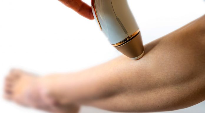 Frau wendet ein IPL-Gerät zur dauerhaften Haarentfernung am Unterschenkel an. Nahaufnahme der Behandlung, Fokus auf Haut und Handgerät für glatte, haarfreie Beine.