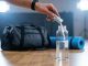 Welches Elektrolyt sollte ich kaufen? Hand gibt Elektrolytpulver in eine Wasserflasche vor dem Sport. Im Hintergrund liegen Sporttasche und Trainingsmatte. Symbolbild für Elektrolytgetränke, Mineralstoffausgleich und Regeneration nach körperlicher Belastung.