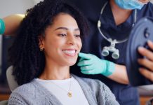 Patientin betrachtet beim Termin in einer Zahnarztpraxis ihr Lächeln im Spiegel, während Fachpersonal berät – Symbolbild für kieferorthopädische Beratung und ästhetische Zahnbehandlung.