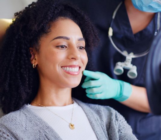 Patientin betrachtet beim Termin in einer Zahnarztpraxis ihr Lächeln im Spiegel, während Fachpersonal berät – Symbolbild für kieferorthopädische Beratung und ästhetische Zahnbehandlung.