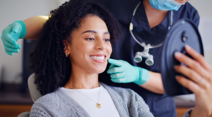 Patientin betrachtet beim Termin in einer Zahnarztpraxis ihr Lächeln im Spiegel, während Fachpersonal berät – Symbolbild für kieferorthopädische Beratung und ästhetische Zahnbehandlung.