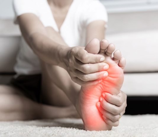 Person sitzt auf dem Boden und hält schmerzhaft die Fußsohle, der Bereich des Vorfußes ist rot markiert – Symbolbild für Fußschmerzen durch Fehlstellungen wie Spreiz- oder Plattfuß.