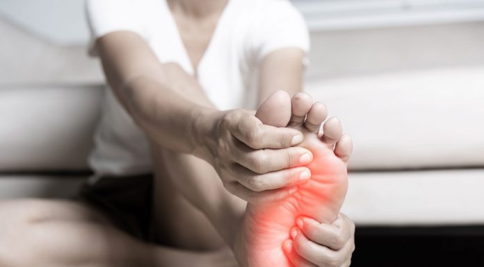 Person sitzt auf dem Boden und hält schmerzhaft die Fußsohle, der Bereich des Vorfußes ist rot markiert – Symbolbild für Fußschmerzen durch Fehlstellungen wie Spreiz- oder Plattfuß.