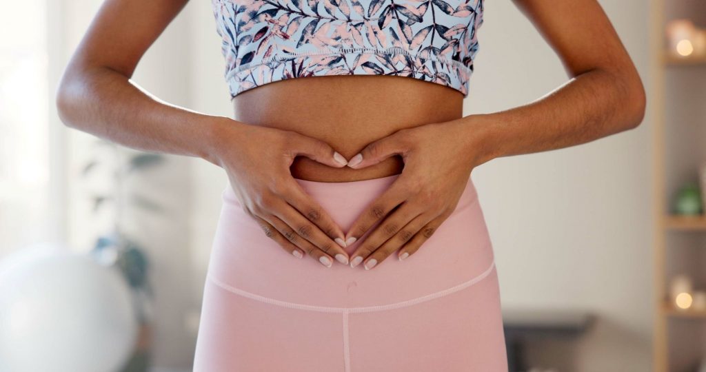 Frau formt mit den Händen ein Herz über dem Unterbauch – Symbol für ein gesundes Bauchgefühl, Darmgesundheit und ganzheitliches Wohlbefinden.