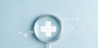 Gesundheitsvorsorge als Schlüssel zu mehr Lebensqualität Hand hält eine Lupe über einem medizinischen Kreuz, umgeben von digitalen Gesundheitssymbolen als Motiv für Gesundheitsvorsorge und Prävention.