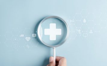 Hand hält eine Lupe über einem medizinischen Kreuz, umgeben von digitalen Gesundheitssymbolen als Motiv für Gesundheitsvorsorge und Prävention.