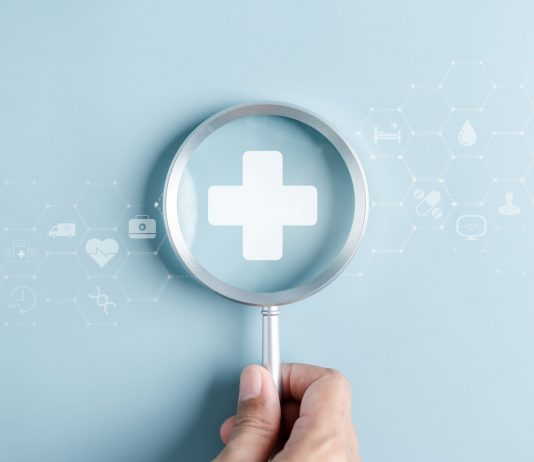 Gesundheitsvorsorge als Schlüssel zu mehr Lebensqualität Hand hält eine Lupe über einem medizinischen Kreuz, umgeben von digitalen Gesundheitssymbolen als Motiv für Gesundheitsvorsorge und Prävention.
