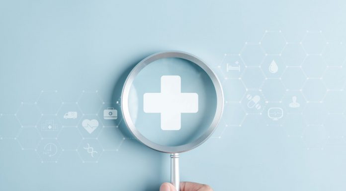 Gesundheitsvorsorge als Schlüssel zu mehr Lebensqualität Hand hält eine Lupe über einem medizinischen Kreuz, umgeben von digitalen Gesundheitssymbolen als Motiv für Gesundheitsvorsorge und Prävention.