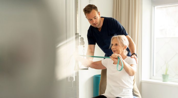 Hausbesuche und Praxisphysiotherapie: Was Ärzte ihren Patienten empfehlen sollten Physiotherapeut unterstützt ältere Patientin beim Training mit Widerstandsband auf einem Gymnastikball in einer hellen Praxis.