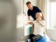 Physiotherapeut unterstützt ältere Patientin beim Training mit Widerstandsband auf einem Gymnastikball in einer hellen Praxis.