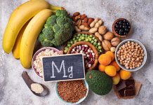 Magnesium bei Stress: Welche Rolle spielt der Mineralstoff für Nerven und Entspannung? Magnesiumreiche Lebensmittel wie Bananen, Nüsse, Hülsenfrüchte, Brokkoli und dunkle Schokolade liegen neben einer Tafel mit Mg-Symbol.