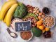 Magnesiumreiche Lebensmittel wie Bananen, Nüsse, Hülsenfrüchte, Brokkoli und dunkle Schokolade liegen neben einer Tafel mit Mg-Symbol.