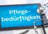 Tablet mit dem Schriftzug „Pflegebedürftigkeit“, Stethoskop, Medikamentenblister und Dokumente als Symbol für Pflegegrad und Pflegeleistungen.