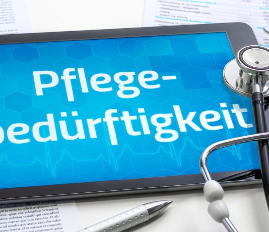 Tablet mit dem Schriftzug „Pflegebedürftigkeit“, Stethoskop, Medikamentenblister und Dokumente als Symbol für Pflegegrad und Pflegeleistungen.