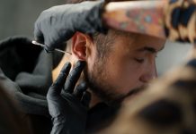 Mann bekommt Piercing am Ohrläppchen, Piercer trägt mit Handschuhen antiseptische Lösung auf – hygienische Vorbereitung vor dem Stechen eines Ohrpiercings in einem Piercingstudio.