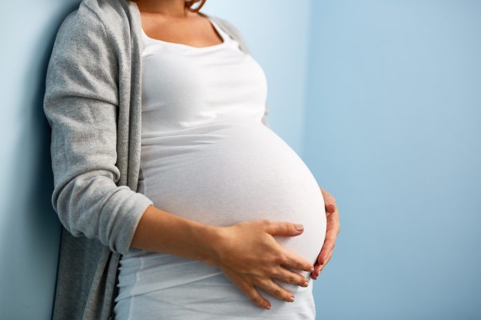 Schwangere Frau kurz vor der Geburt Eine schwangere Frau lehnt an einer Wand und legt ihre Hände auf ihren Bauch.