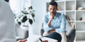 Psychotherapeutische Sitzung: Ein Mann spricht mit einem Therapeuten, der Notizen macht. Thema sind Trauma, Angststörungen und moderne Traumatherapie in ruhiger Praxisumgebung.