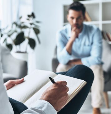 Psychotherapeutische Sitzung: Ein Mann spricht mit einem Therapeuten, der Notizen macht. Thema sind Trauma, Angststörungen und moderne Traumatherapie in ruhiger Praxisumgebung.