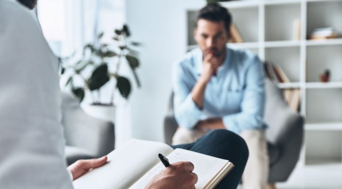 Psychotherapeutische Sitzung: Ein Mann spricht mit einem Therapeuten, der Notizen macht. Thema sind Trauma, Angststörungen und moderne Traumatherapie in ruhiger Praxisumgebung.