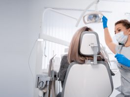 Zahnärztin mit Maske und Handschuhen bereitet in einer hellen Praxis die zahnärztliche Untersuchung einer Patientin auf dem Behandlungsstuhl vor.