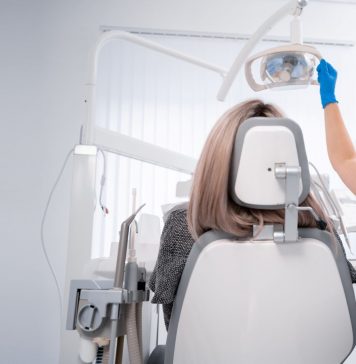 Zahnärztin mit Maske und Handschuhen bereitet in einer hellen Praxis die zahnärztliche Untersuchung einer Patientin auf dem Behandlungsstuhl vor.