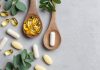 Omega-3-Kapseln und Nahrungsergänzungsmittel auf Holzlöffeln mit grünen Blättern auf hellem Hintergrund. Symbolbild für Fischöl, EPA, DHA, Omega-3-Präparate und Gesundheitsvorsorge.